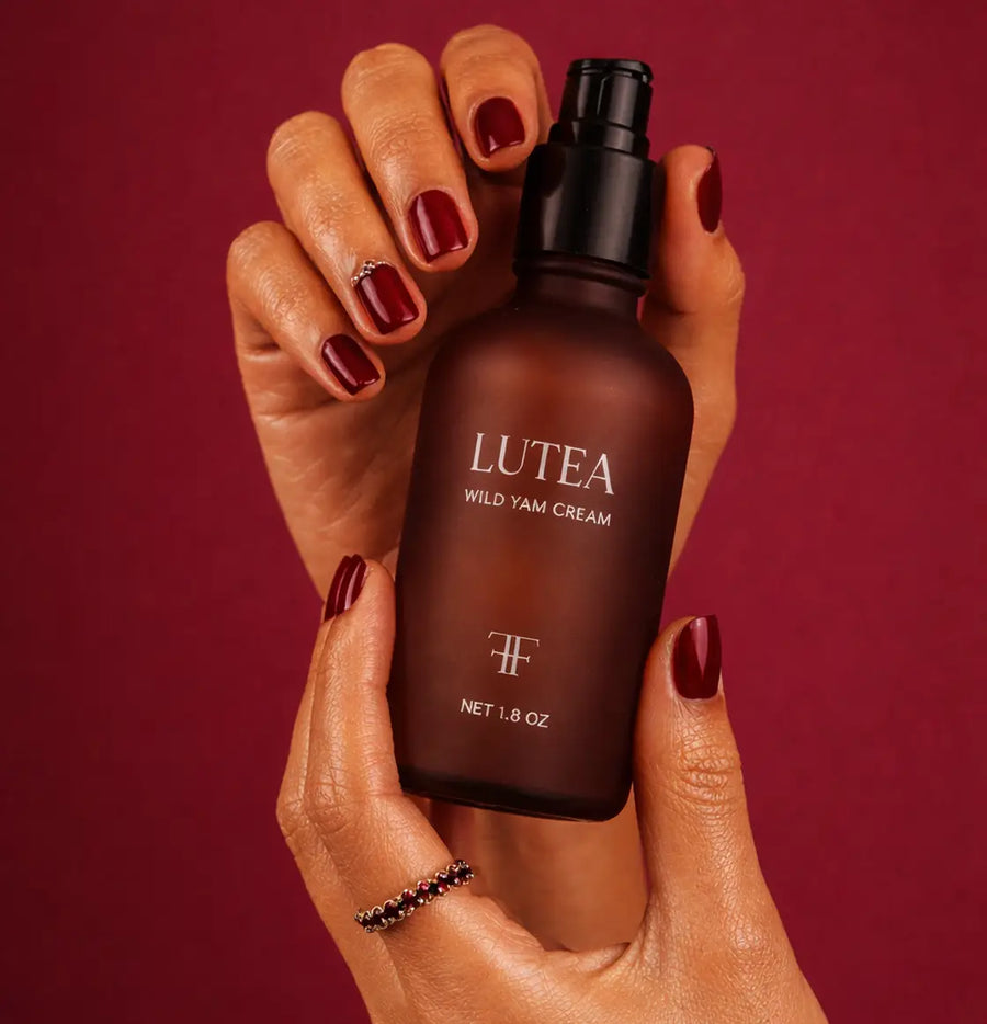 A hand holding the LUTÉA pump bottle against deep red