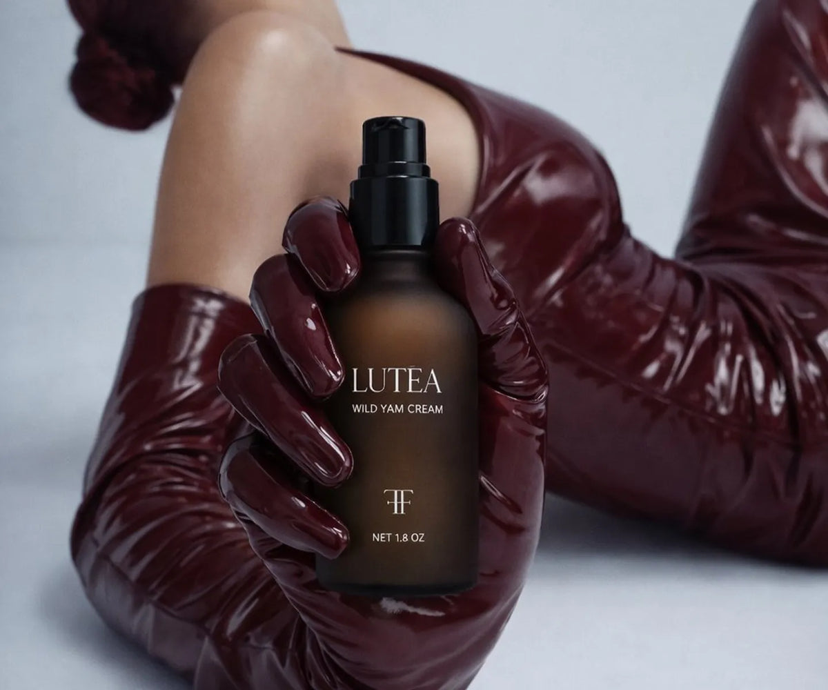 A hand in a burgundy glove holding the LUTÉA pump bottle