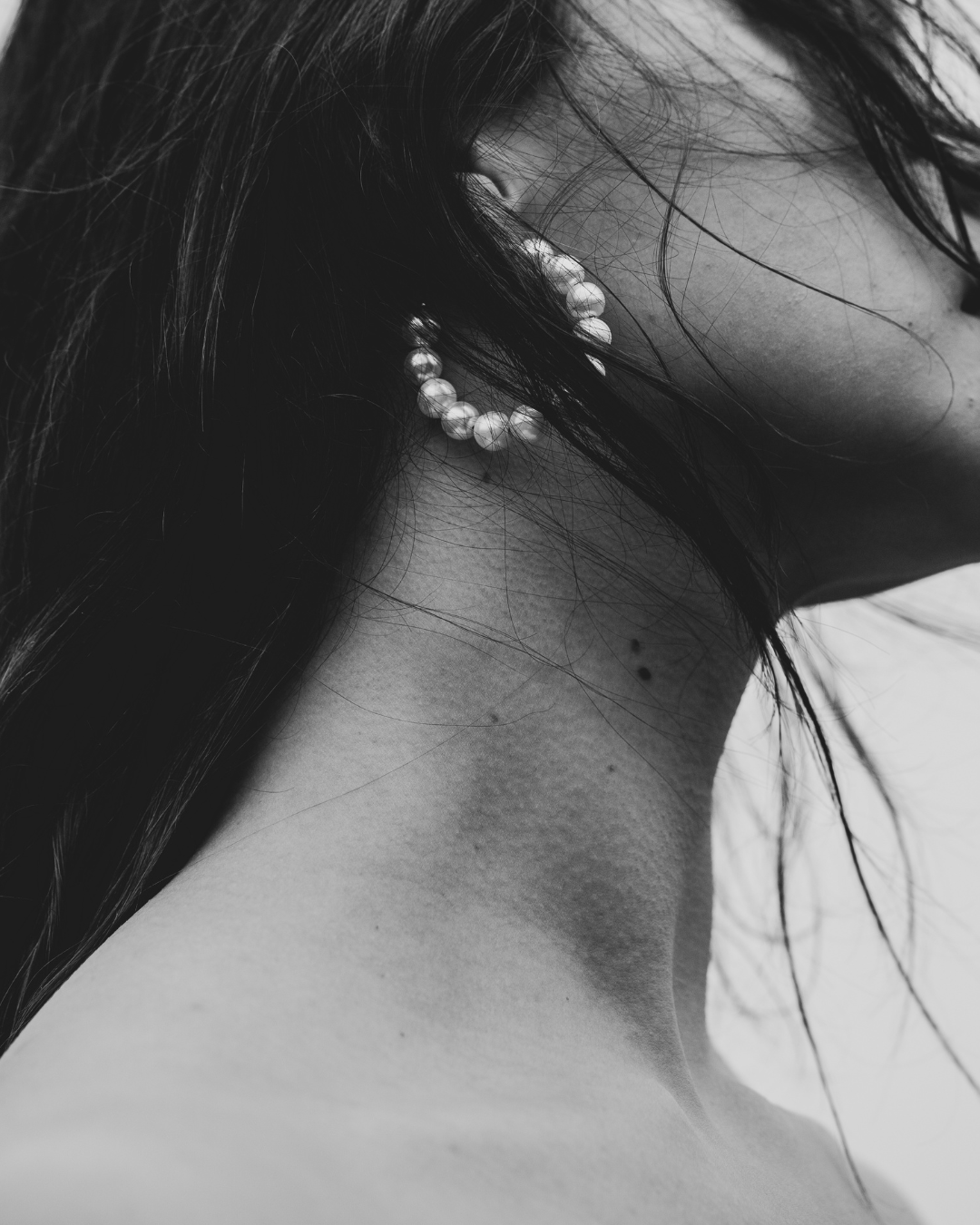 Black and white photo of a person with a hoop earring on their ear.
